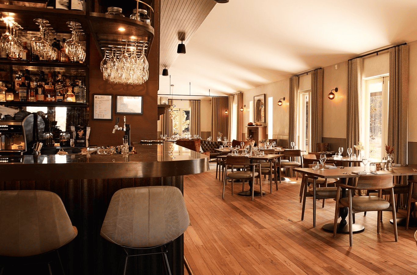 Lot 101 Megalong Restaurant is the perfect destination for food enthusiasts, featuring a modern interior with wooden floors, a stylish bar area, shelves of bottles, cushioned bar stools, and sunlit dining tables in a room with large windows and neutral decor. | Megalong Restaurant