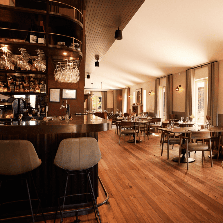 Lot 101 Megalong Restaurant is the perfect destination for food enthusiasts, featuring a modern interior with wooden floors, a stylish bar area, shelves of bottles, cushioned bar stools, and sunlit dining tables in a room with large windows and neutral decor. | Megalong Restaurant