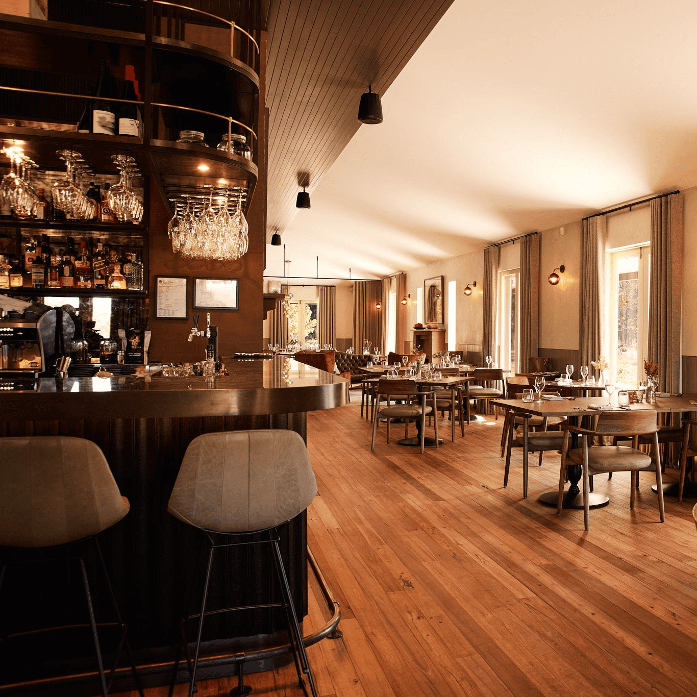 Lot 101 Megalong Restaurant is the perfect destination for food enthusiasts, featuring a modern interior with wooden floors, a stylish bar area, shelves of bottles, cushioned bar stools, and sunlit dining tables in a room with large windows and neutral decor. | Megalong Restaurant