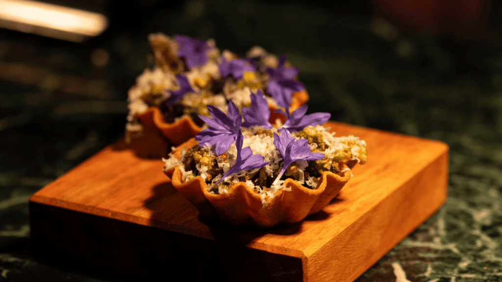 Elegant tart topped with purple edible flowers on a wooden board.
