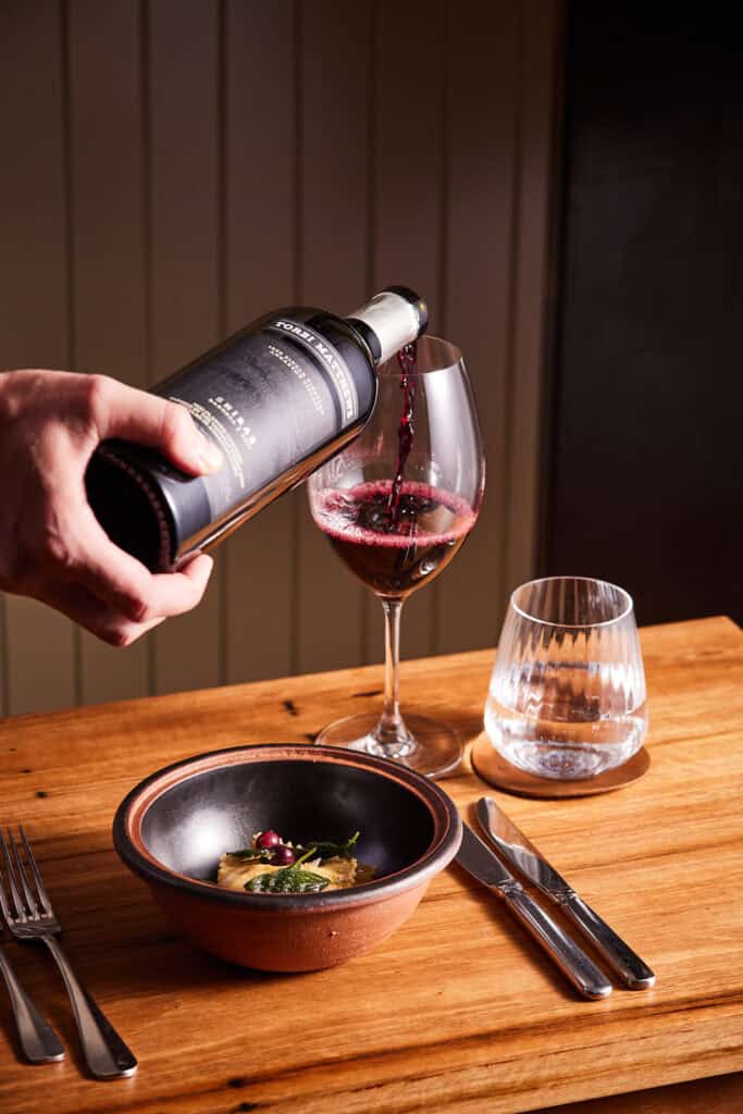 Pouring red wine into a glass at a stylish dining setup.