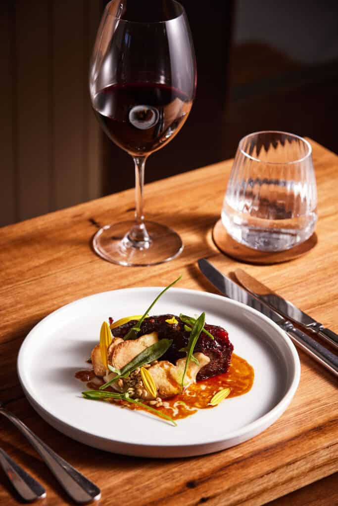 Glass of red wine and gourmet dish on a wooden table at LOT 101.