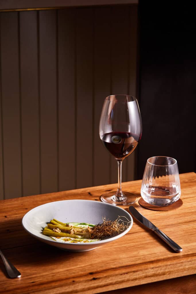 Wine glass, water glass, and plated meal on wooden table at LOT 101.