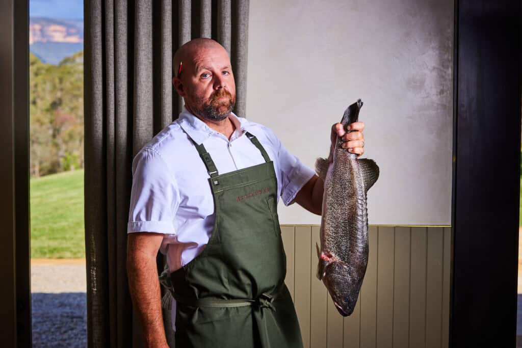 Man with a large fish in a restaurant or market setting.