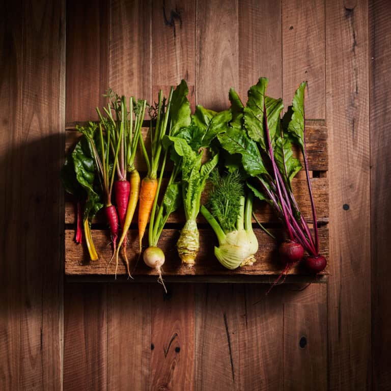 Colorful fresh organic vegetables including carrots, beets, and fennel on wooden shelf.
