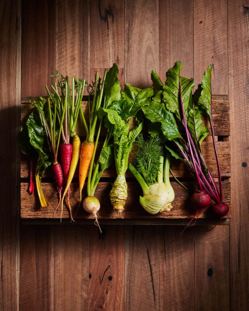 Colorful fresh organic vegetables including carrots, beets, and fennel on wooden shelf.