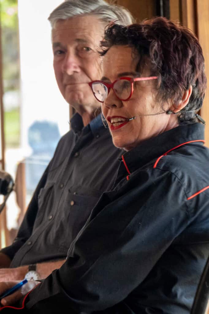 Two people sitting indoors, engaged in conversation, with a blurred background.