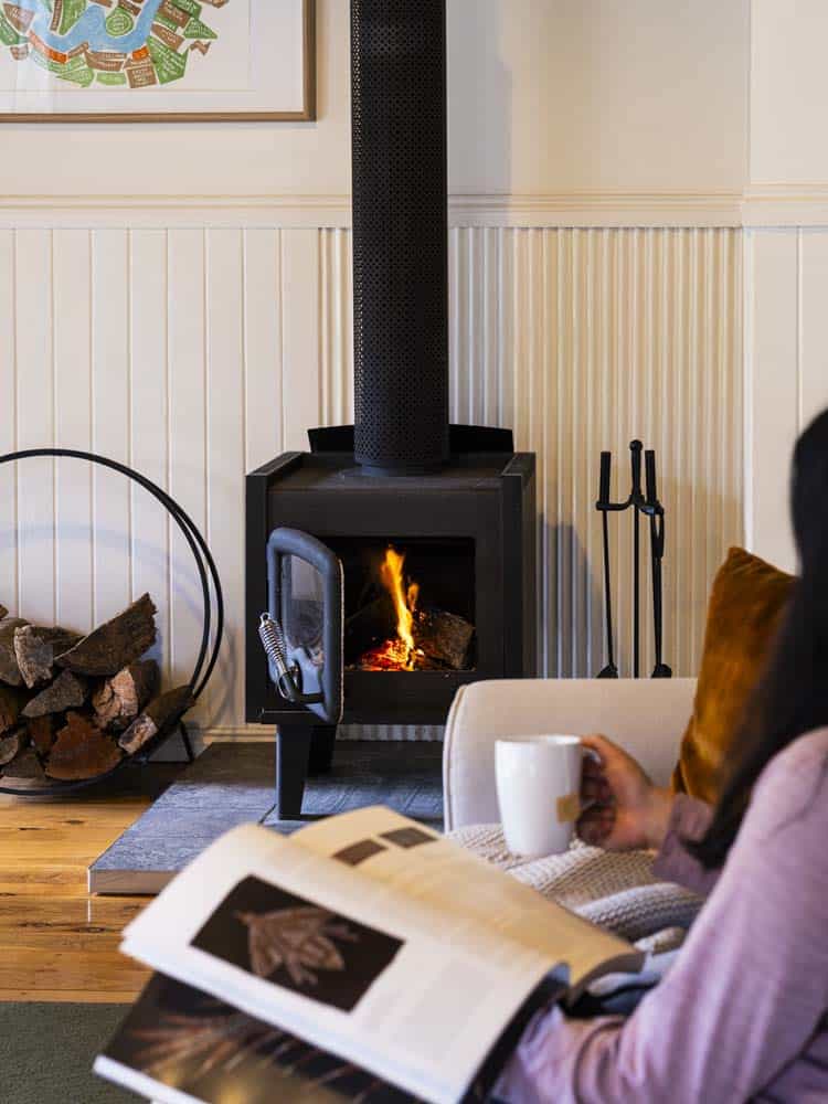 Warm living room with a wood-burning fireplace and a person reading a magazine.