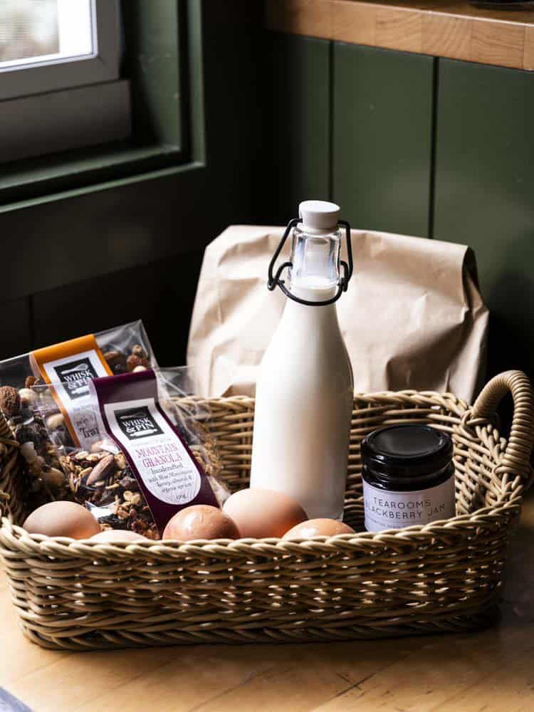 Basket with eggs, jam, milk bottle, and snacks on a kitchen counter.