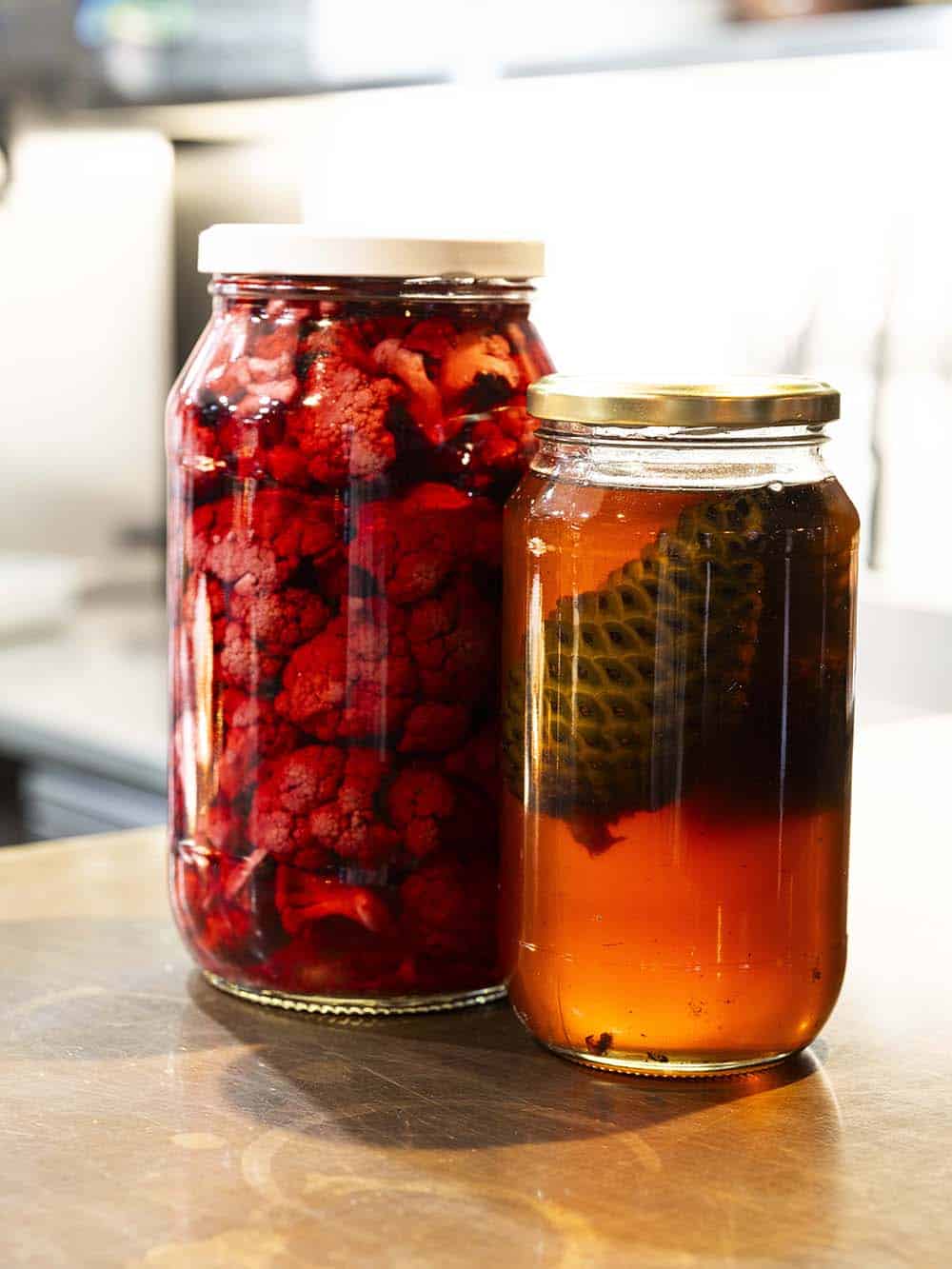 Two glass jars with berry and herbal infusions on a kitchen counter.