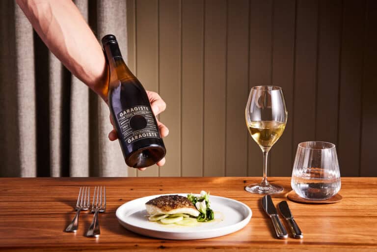 Wine being poured over a fish dish at a stylish dining table.
