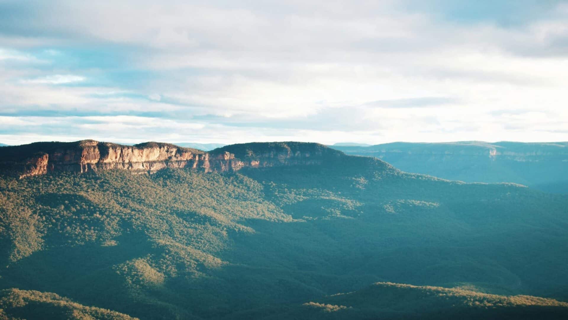 Panoramic view of mountains with lush greenery and cloudy sky.