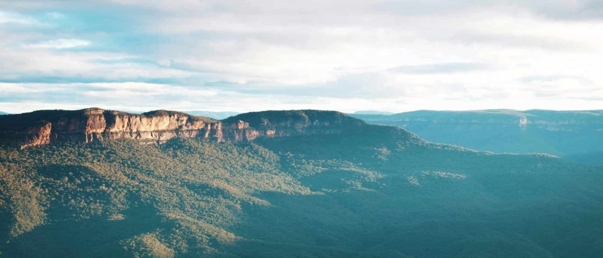 Panoramic view of mountains with lush greenery and cloudy sky.