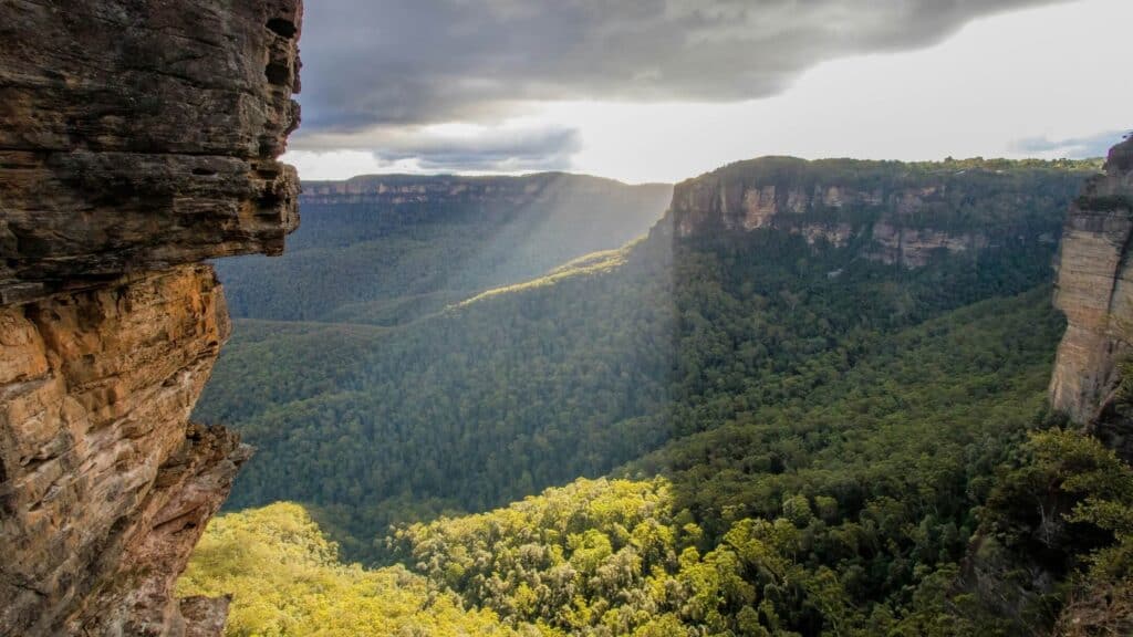 Scenic view of a lush green canyon with cliffs and cloudy sky.