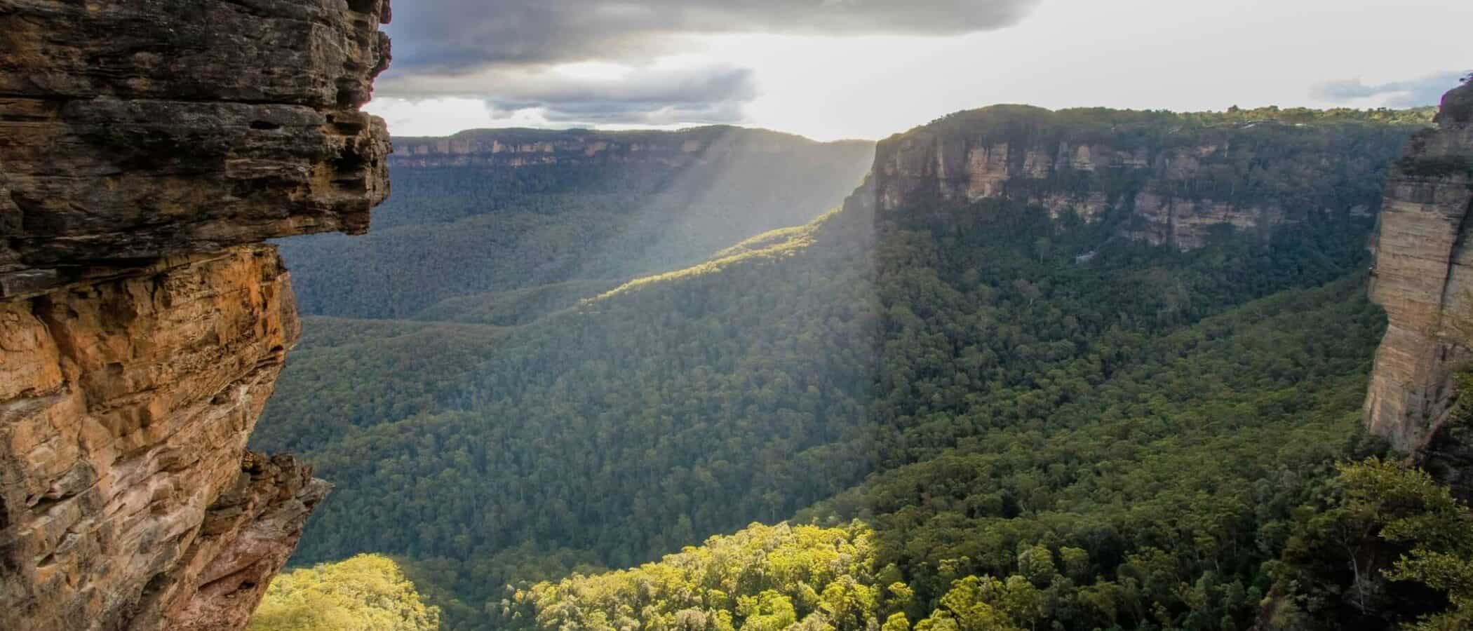Scenic view of a lush green canyon with cliffs and cloudy sky.
