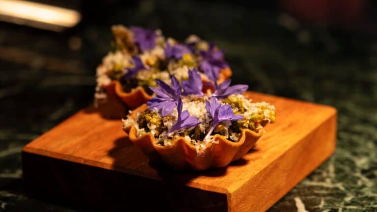 Mini tarts decorated with purple flowers on a wooden board.