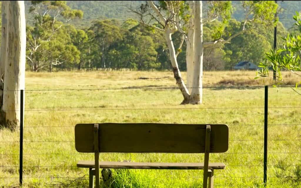 Scenic farm gate with bench and fencing in lush green landscape.