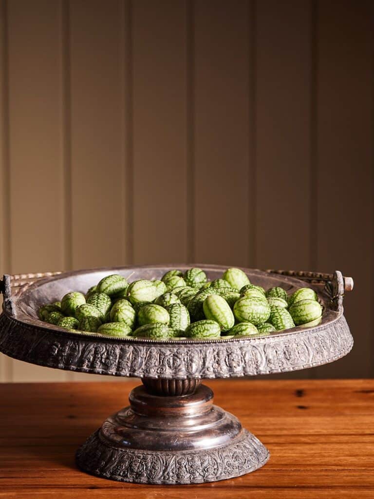 Vintage silver tray filled with green watermelons on wooden table.