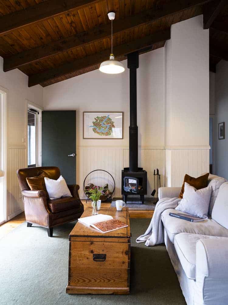 Interior of a cozy living room with a wood stove, sofa, armchair, and wooden ceiling.