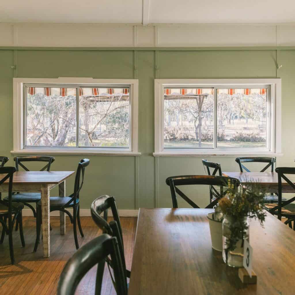 Interior of a tea room with wooden tables, black chairs, and large windows with striped curtains.