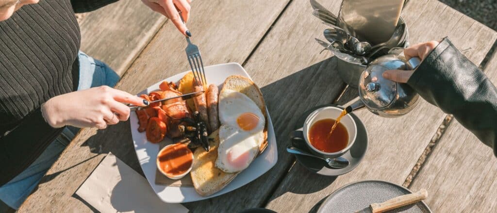 People enjoying breakfast outdoors with eggs, bacon, and tea at a tea room.