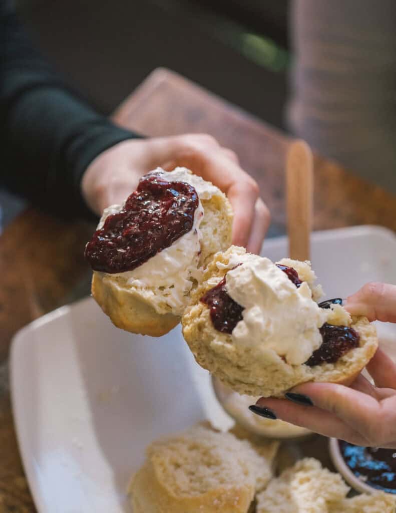 Close-up of hands holding freshly baked scones with jam and cream.